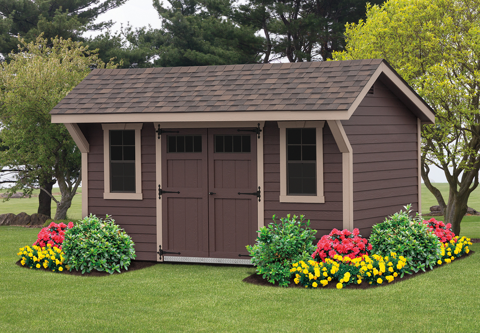 A quaint brown garden shed surrounded by colorful flowers and greenery, set against a backdrop of trees and open lawn.